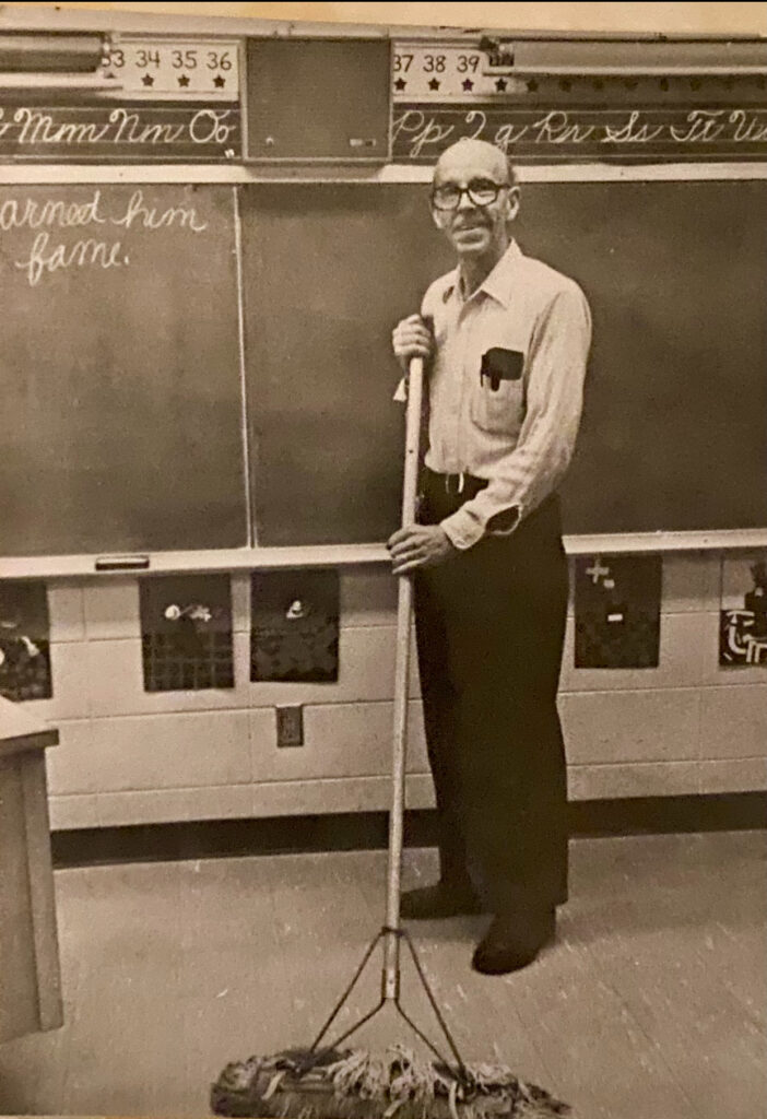 Johnny Mullins, janitor at Wilder Elementary School, standing with sweeping broom for promo photo by magazine photographer in early 1980's